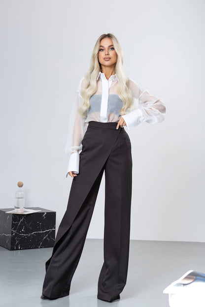 Woman wearing a white blouse with sheer sleeves and black pants on a plain background