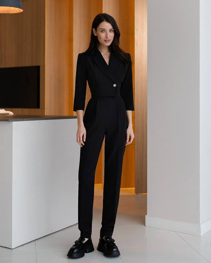 Woman wearing a black suit standing in an indoor setting with wooden paneling.