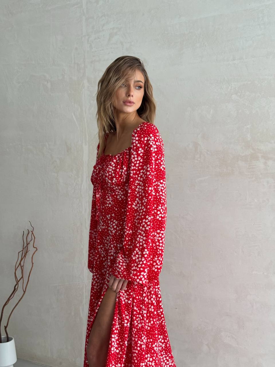 Woman wearing a red floral dress against a plain wall