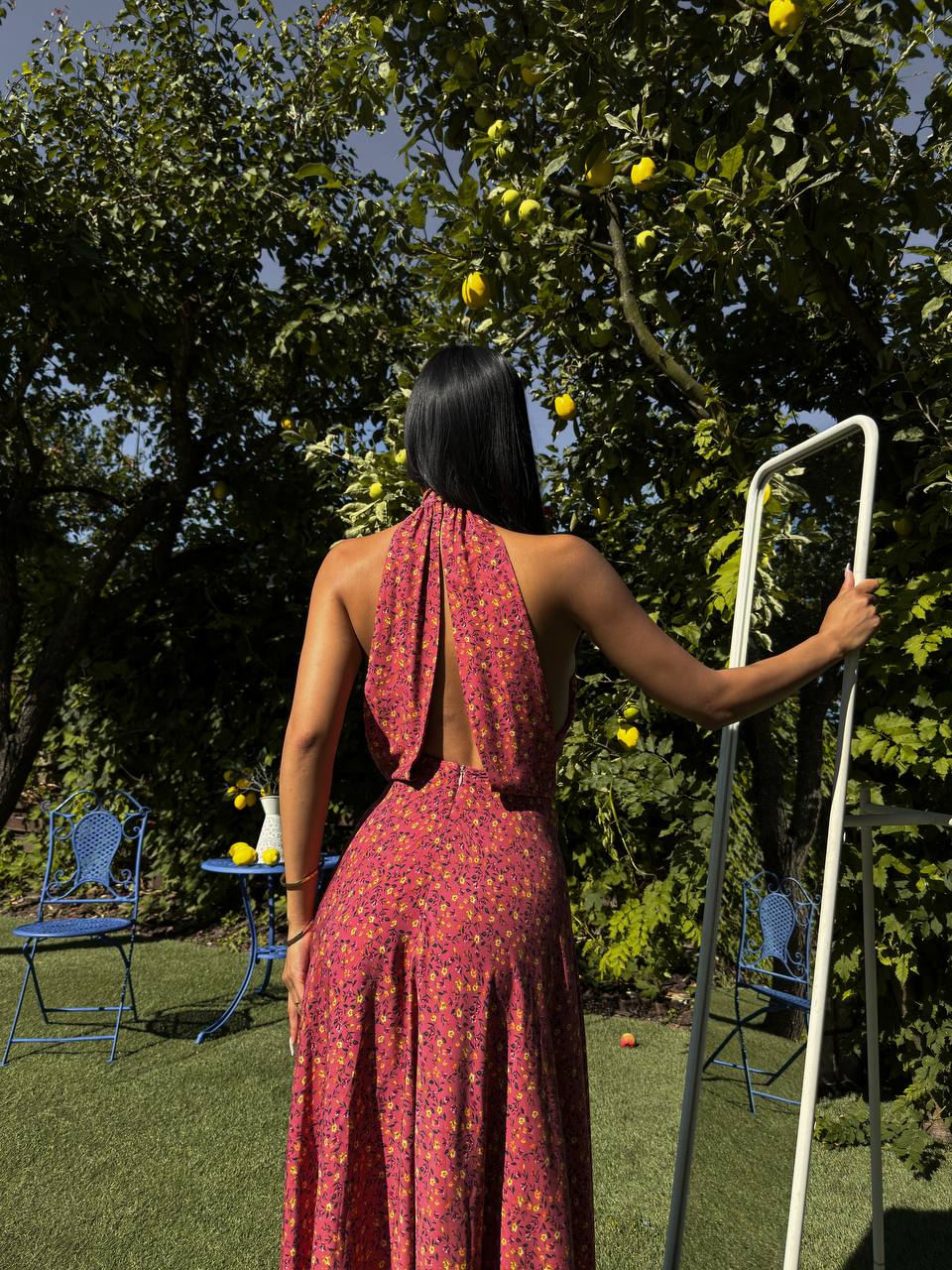 Woman in a red dress standing in a garden with trees and chairs.