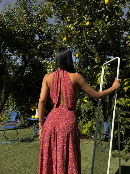 Woman in a red dress standing in a garden with trees and chairs.
