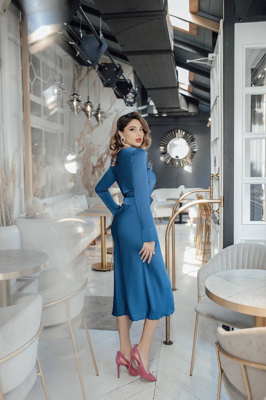 Woman in a blue dress standing in a modern restaurant interior.