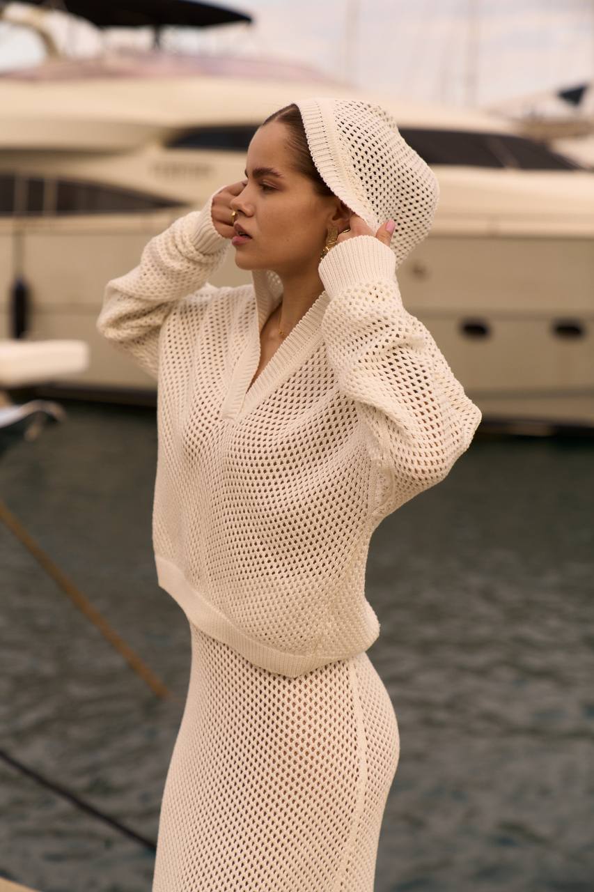 Woman wearing a beige knit outfit with a matching headscarf by a boat.
