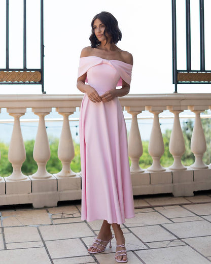 Woman in a pink off-shoulder dress standing on a balcony with a scenic background