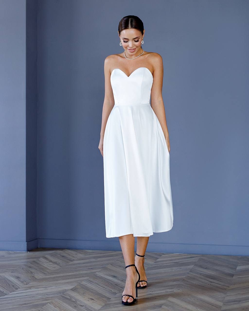 Woman wearing a white strapless dress against a blue wall.