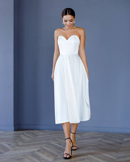 Woman wearing a white strapless dress against a blue wall.