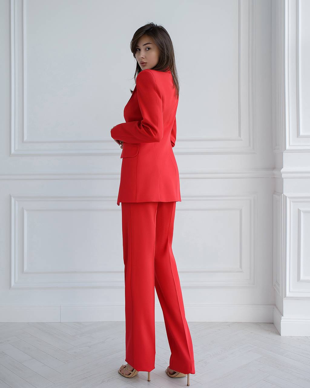Woman wearing a red suit standing against a white wall.