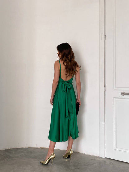 Woman in a green dress standing against a white wall.