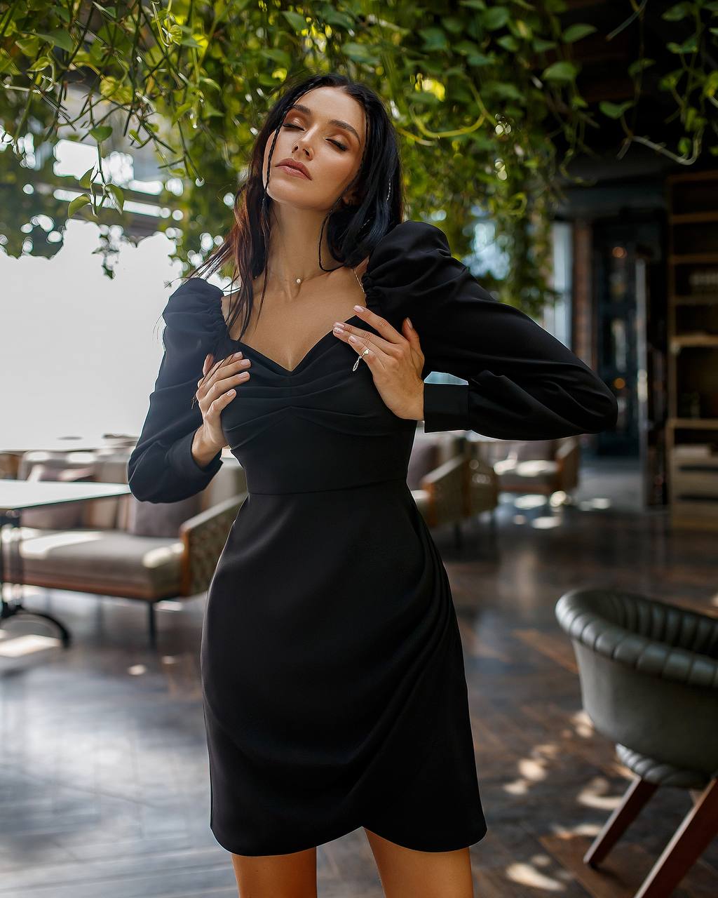 Woman in a black dress standing in an outdoor setting with greenery.