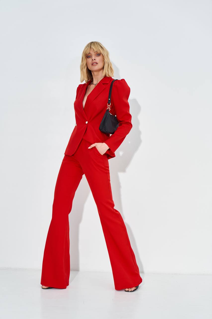 Woman wearing a red suit with a black handbag against a white background