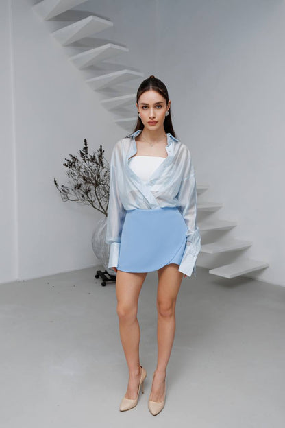 Woman in light blue outfit standing in a minimalistic room with white walls and a staircase.
