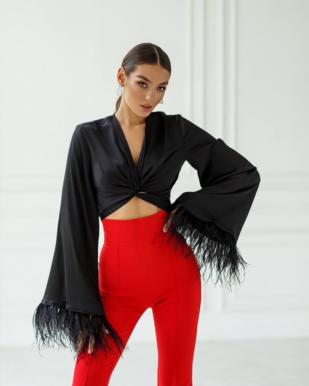 Woman wearing a black fringed top and red pants against a white background