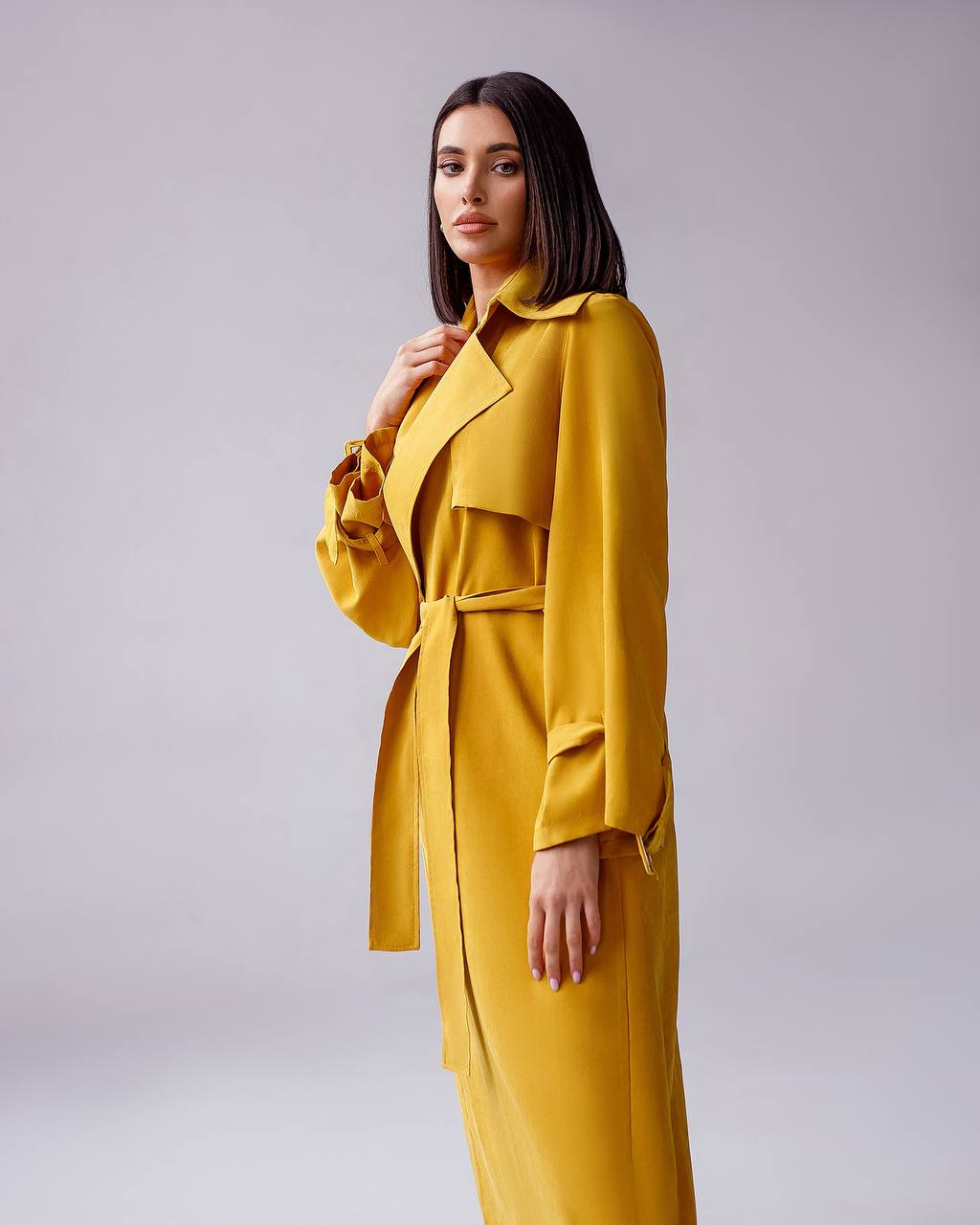 Woman wearing a yellow trench coat against a plain background