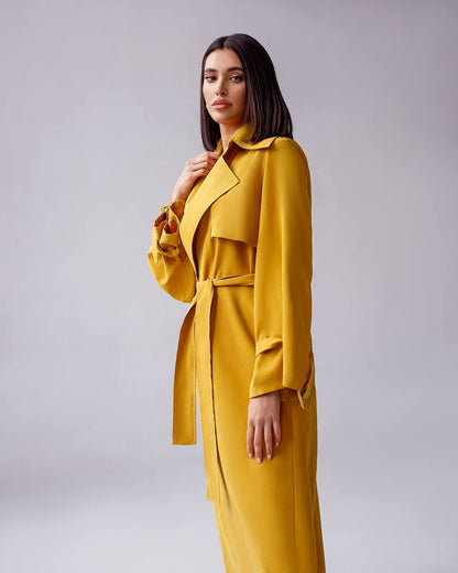 Woman wearing a yellow trench coat against a plain background