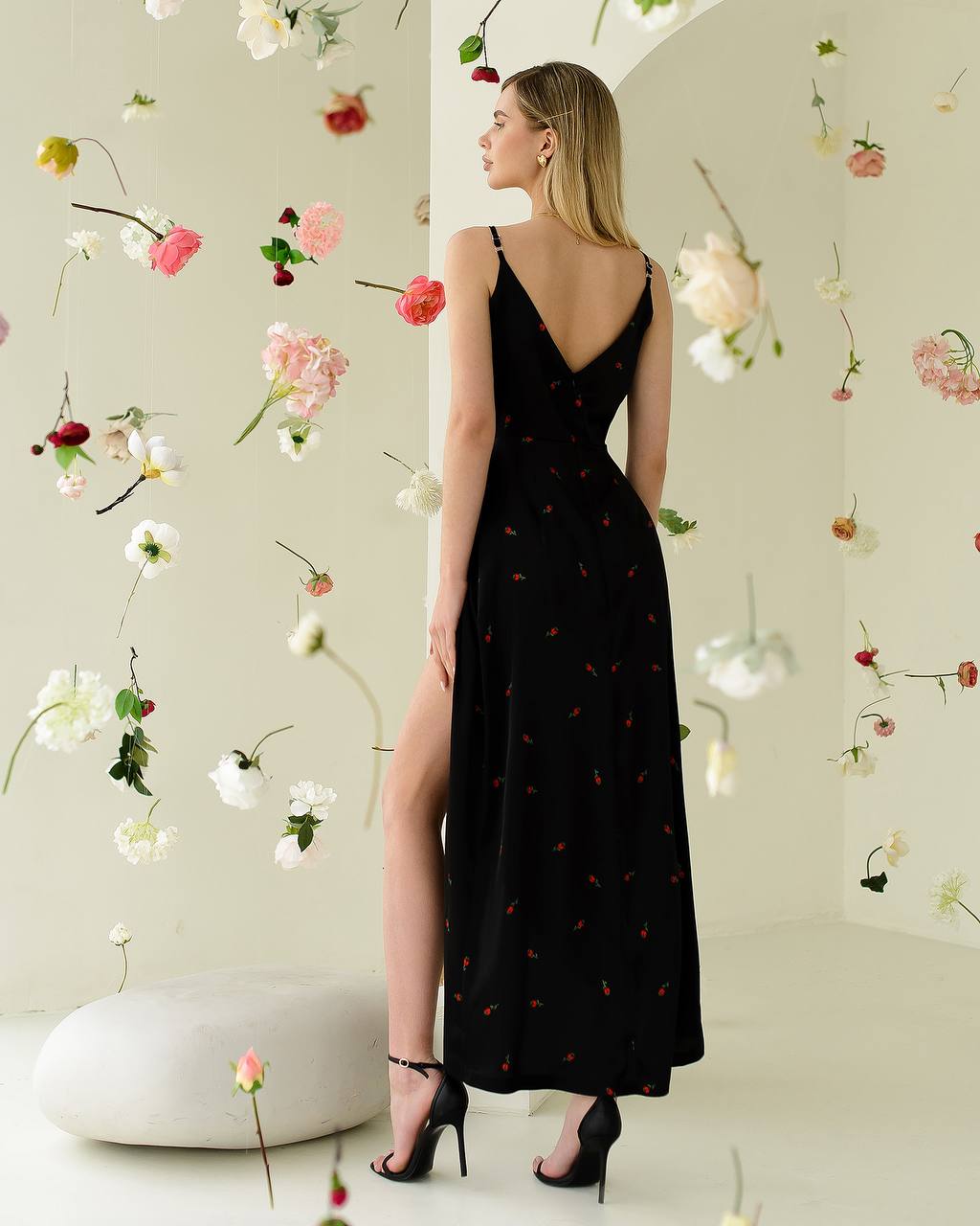 Woman in a black dress with floral decorations on a light-colored wall.