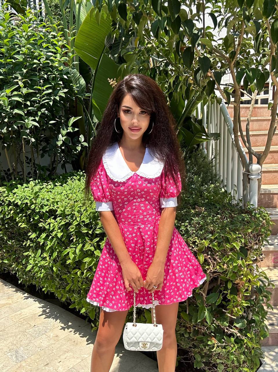 Woman in a pink polka dot dress standing outdoors with greenery in the background