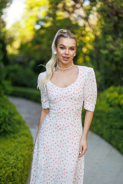 Woman in a floral dress standing outdoors with greenery in the background