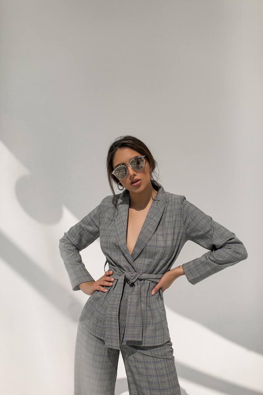 Woman wearing a gray checkered suit with sunglasses against a white background