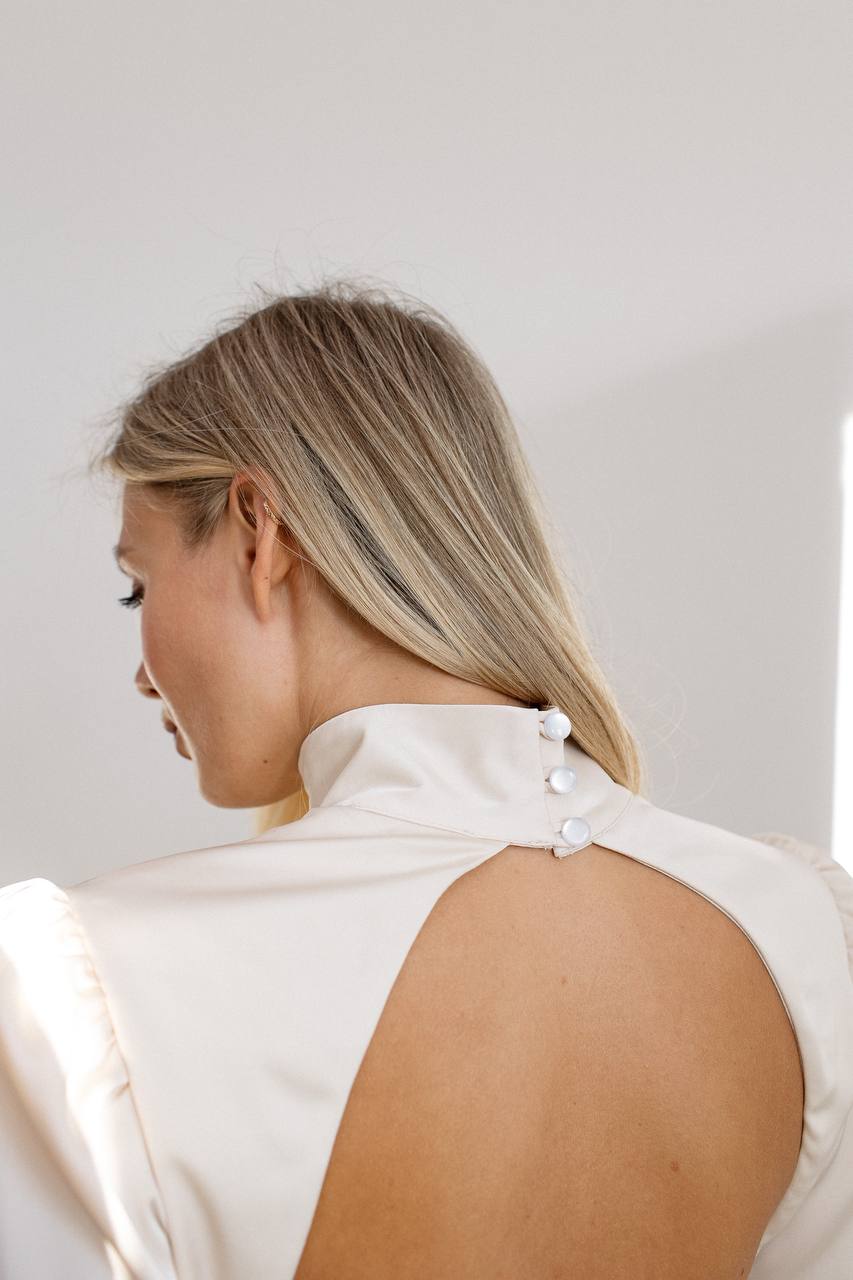 Person wearing a white sleeveless top with a high neckline against a plain background