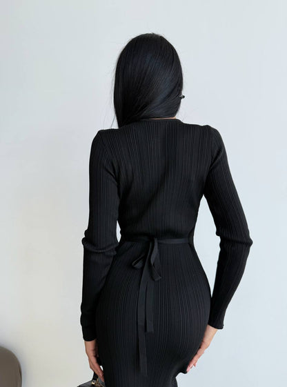 Person wearing a black ribbed dress with long sleeves against a white background