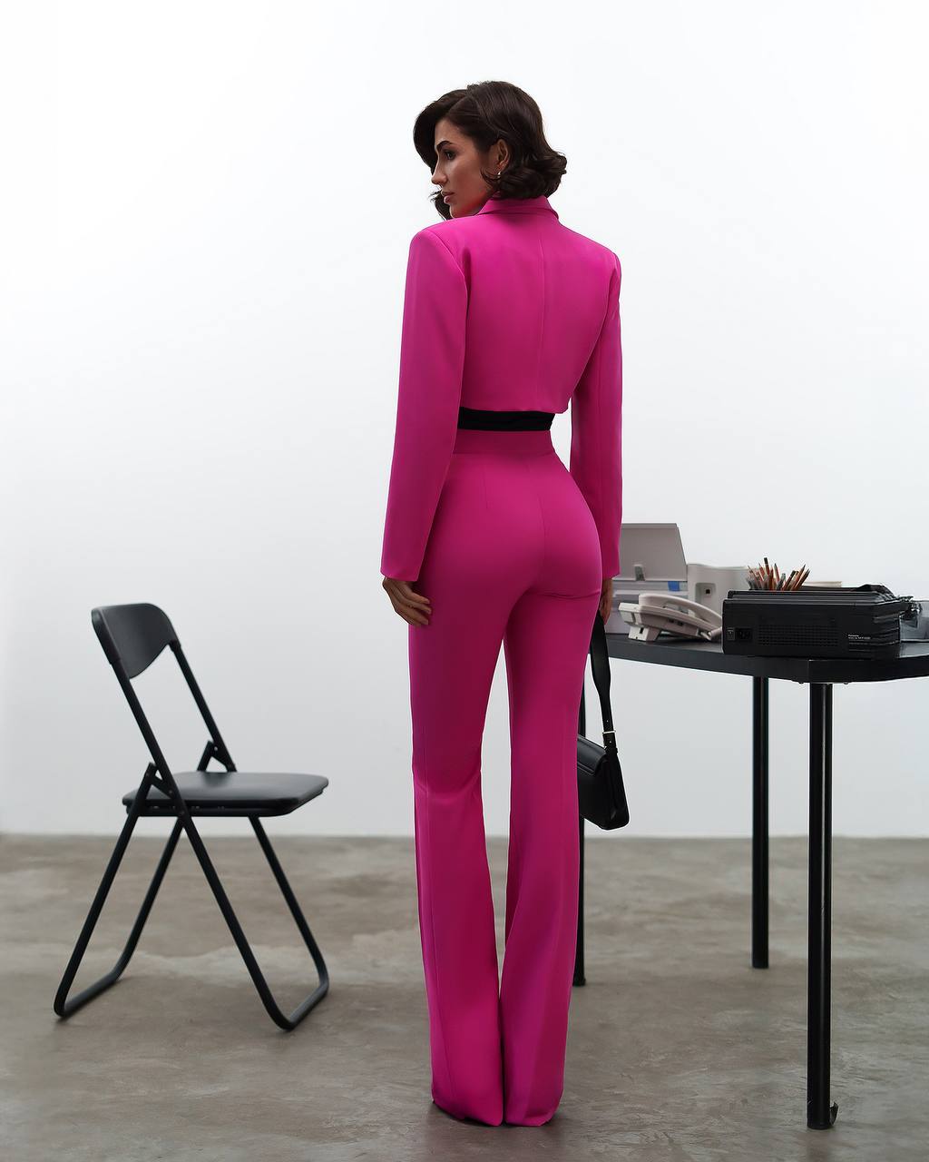Person wearing a bright pink jumpsuit in an indoor setting with a chair and table.