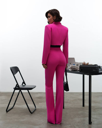 Person wearing a bright pink jumpsuit in an indoor setting with a chair and table.