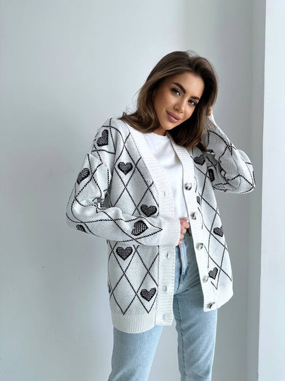 Woman wearing a white cardigan with black heart patterns on a plain background