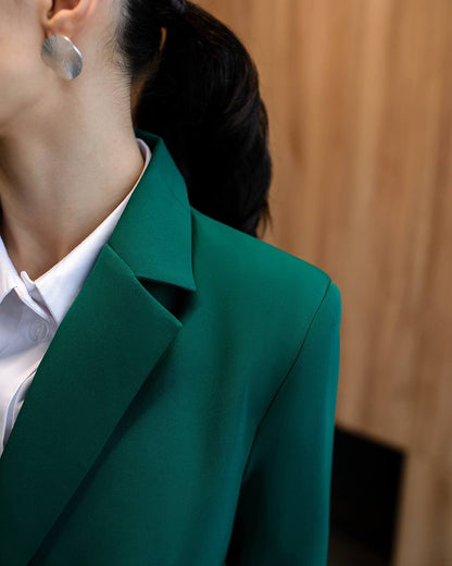 Person wearing a green blazer over a white shirt with a blurred background