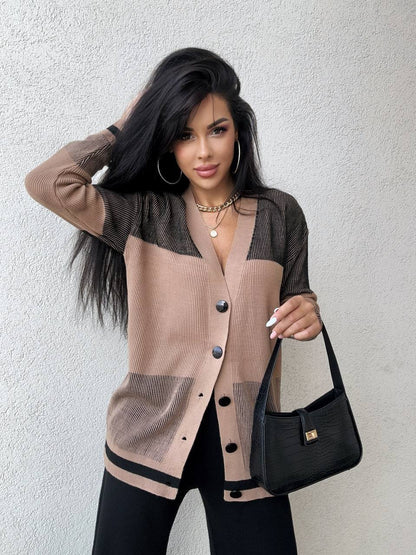Woman wearing a beige and black cardigan holding a black handbag against a light gray background