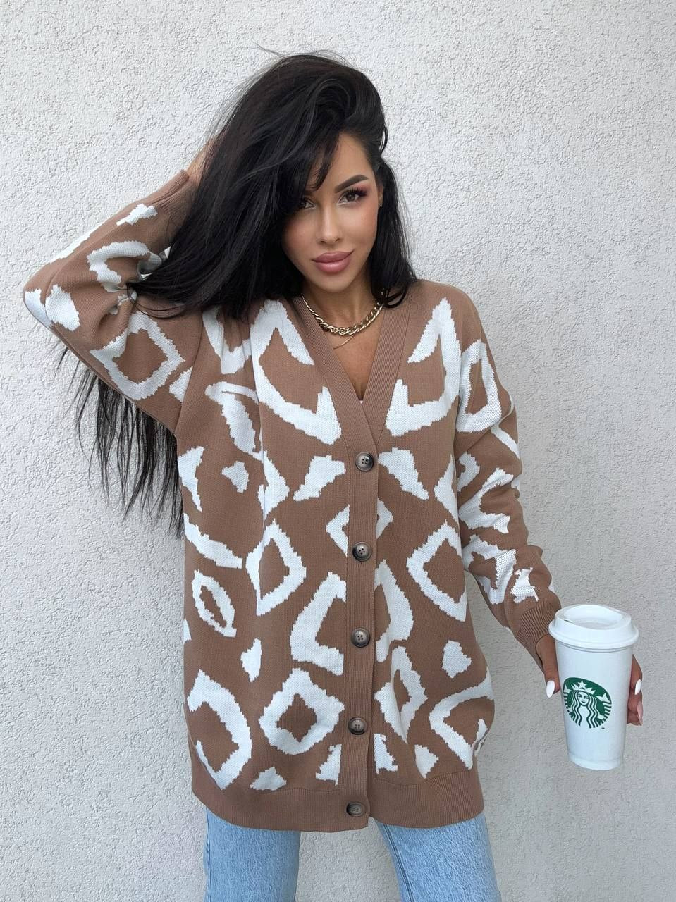 Woman wearing a patterned brown cardigan holding a Starbucks cup against a plain background