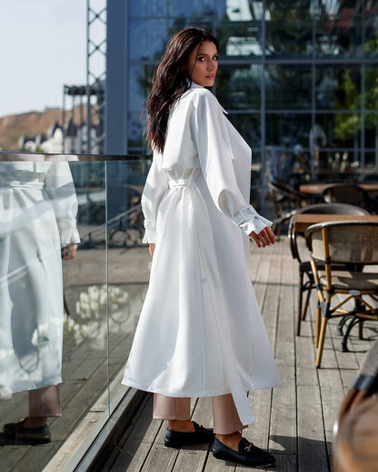 Woman in a white dress standing on a wooden deck with glass walls.