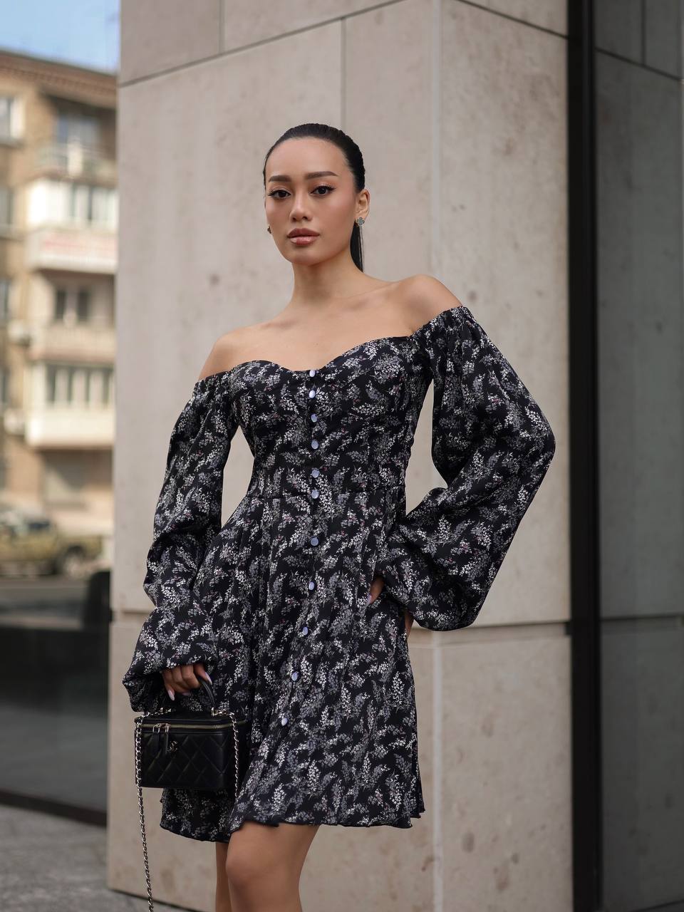 Woman in a black and white patterned off-shoulder dress standing against a concrete wall.