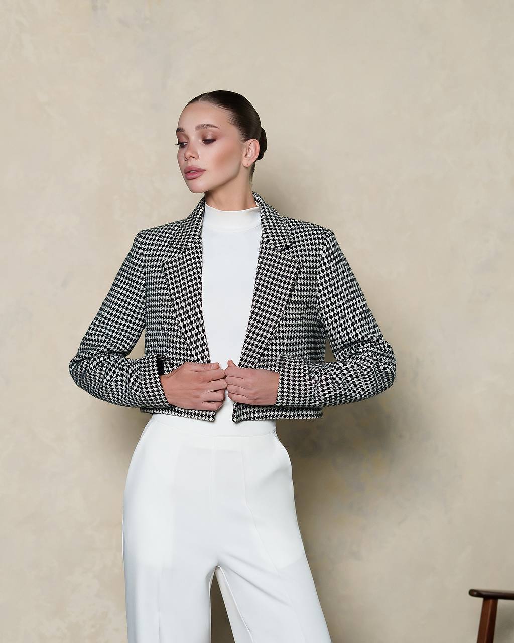Woman wearing a black and white checkered jacket over a white top and pants against a beige background