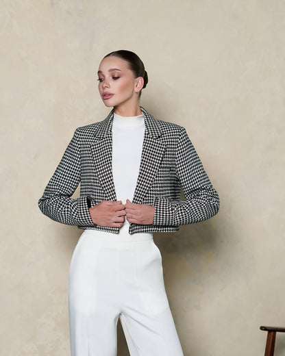 Woman wearing a black and white checkered jacket over a white top and pants against a beige background