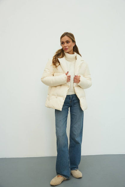 Woman wearing a white puffer jacket and blue jeans against a plain background