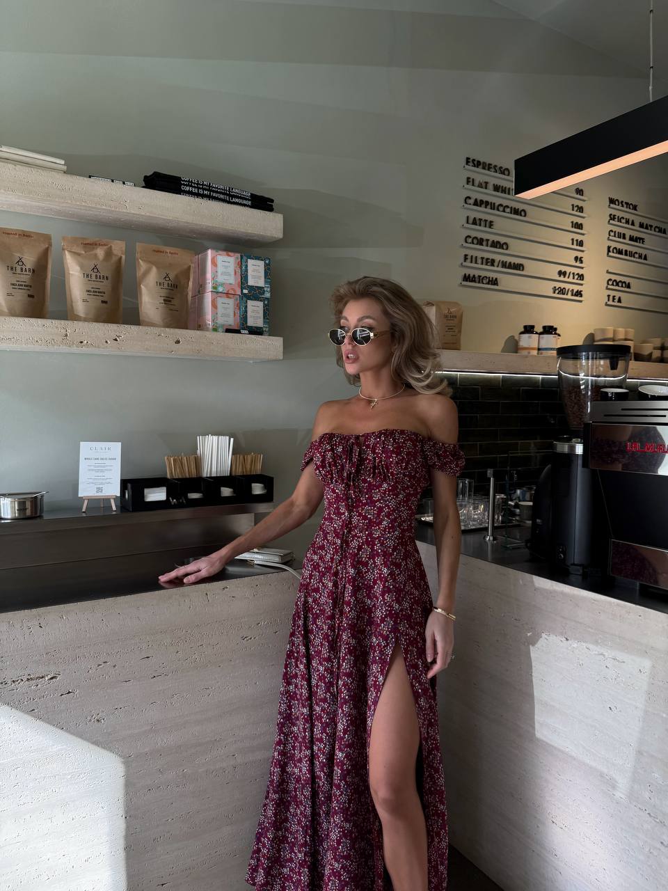 Woman in a burgundy off-shoulder dress standing in a coffee shop.