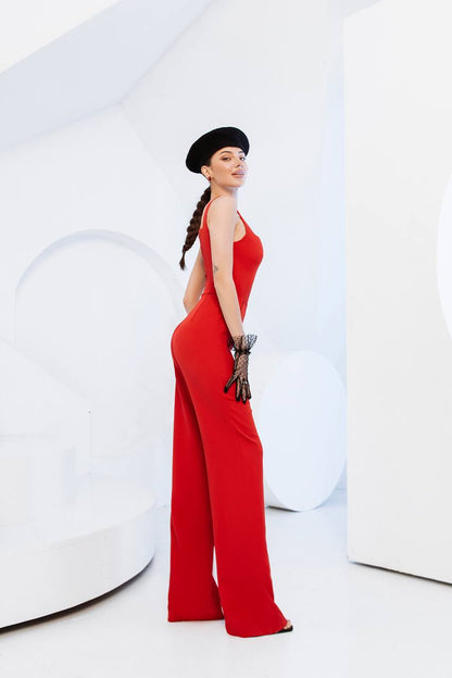 Woman in a red jumpsuit and black hat posing against a white background