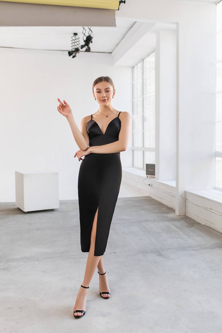Woman wearing a black dress with a high slit in a minimalistic room.