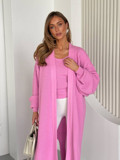 Woman wearing a pink outfit with a long cardigan and matching top, standing against a white background.