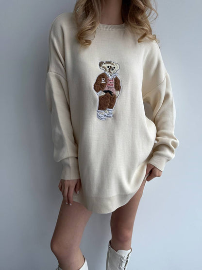 Person wearing a cream sweater with a bear graphic design on a plain background