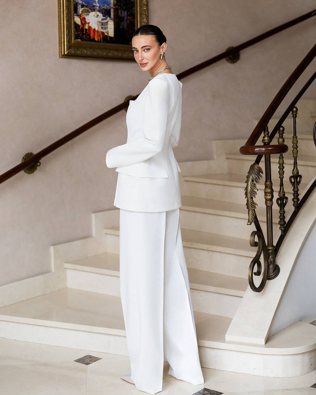 Woman in a white suit standing on a staircase with a painting in the background