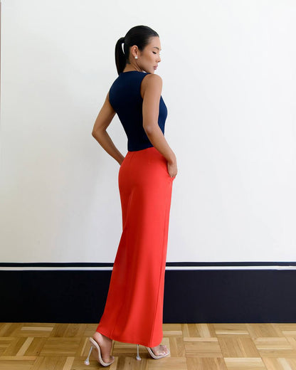 Woman wearing a black top and red pants standing against a white wall.