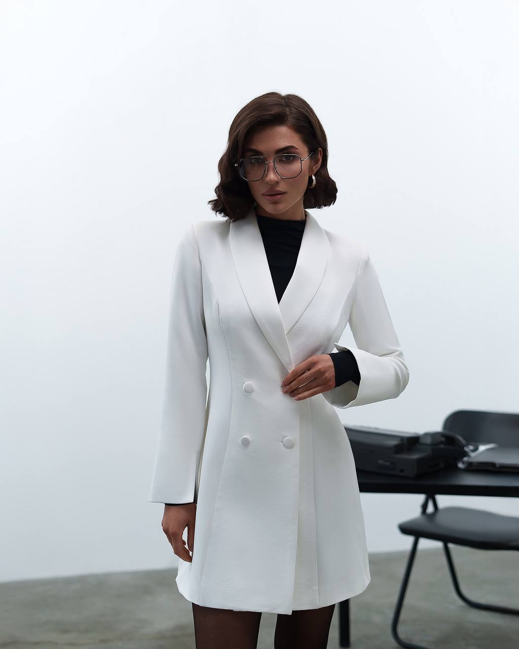 Woman wearing a white blazer over a black top in an indoor setting.