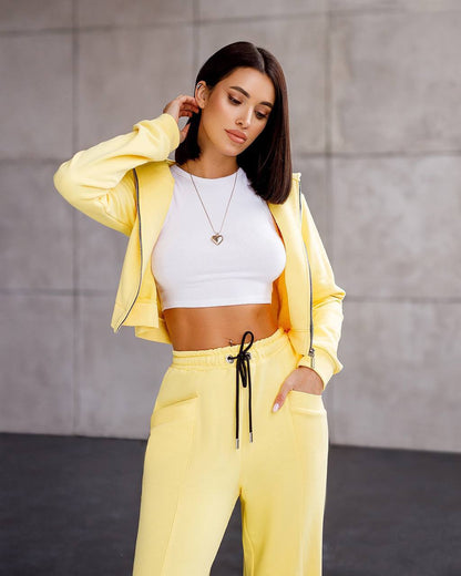 Woman wearing a yellow tracksuit with a white top against a gray background