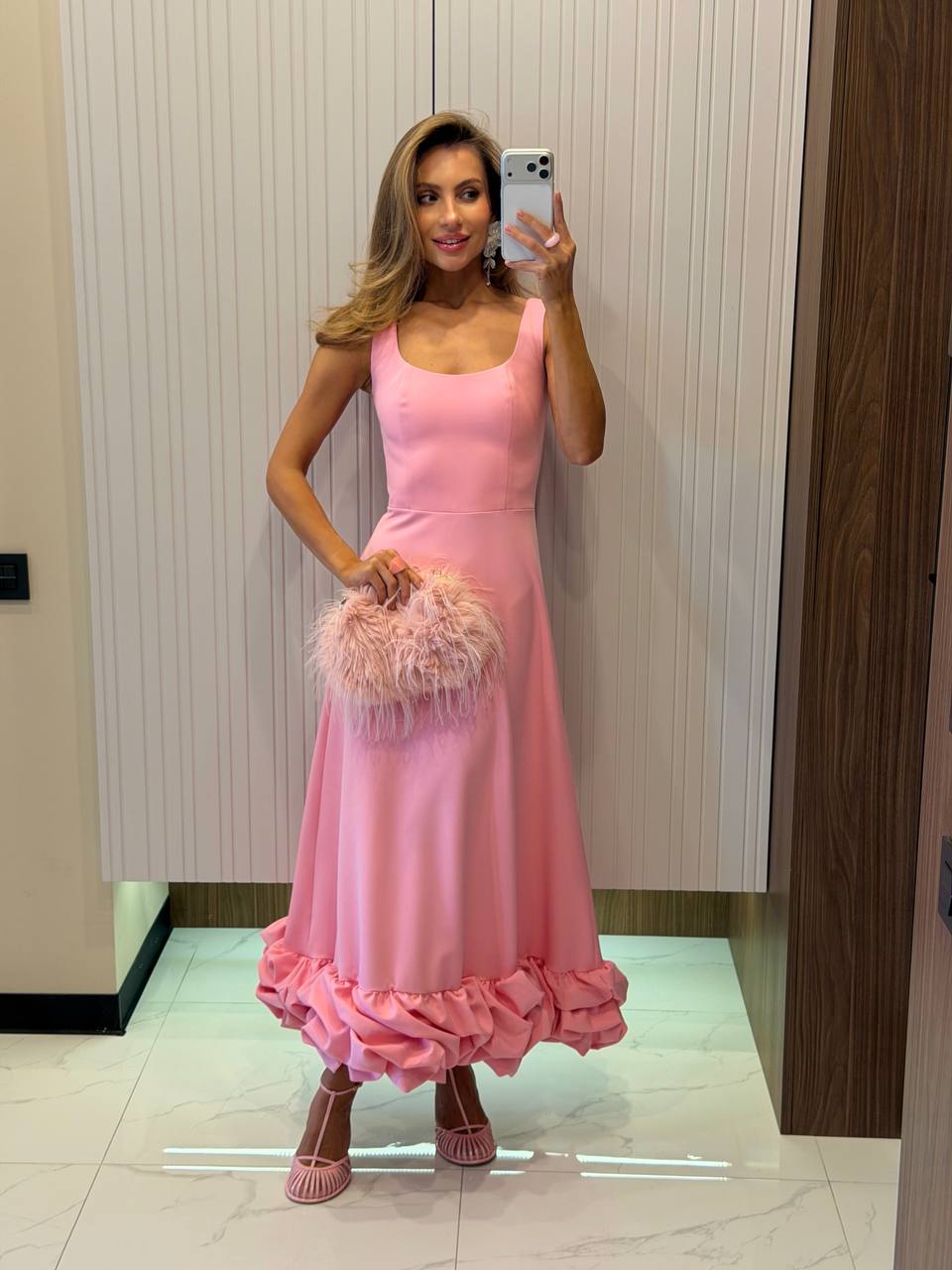 Woman in a pink dress taking a mirror selfie in an elevator.