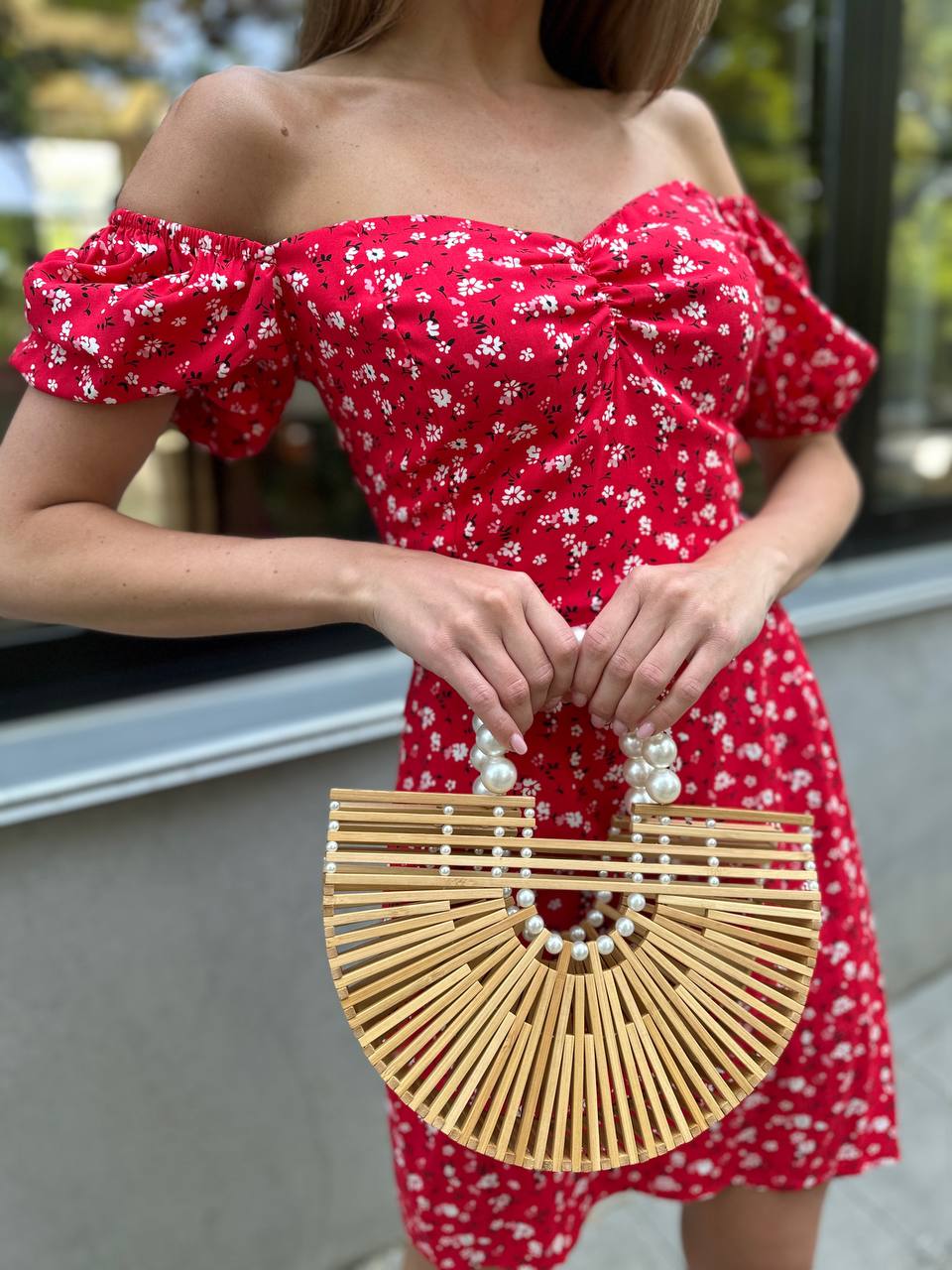 Person wearing a red floral dress holding a bamboo handbag with pearl details.