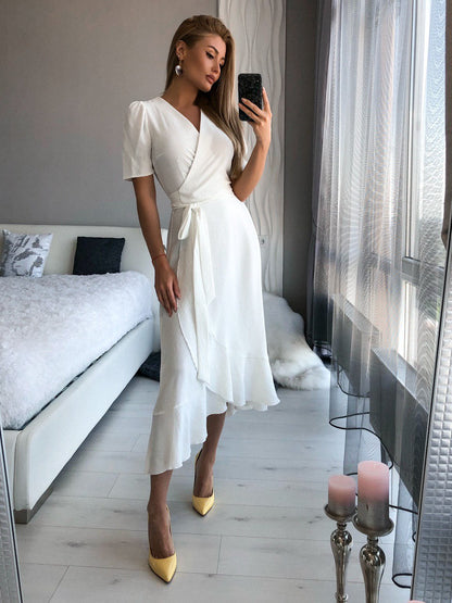 Woman in a white dress taking a mirror selfie in a modern room.