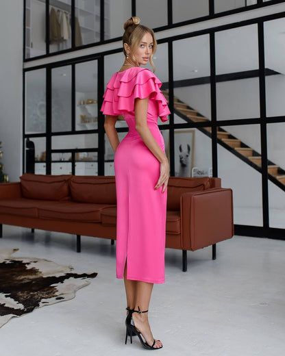 Woman in a bright pink dress standing in a modern interior setting with a brown sofa and glass wall.