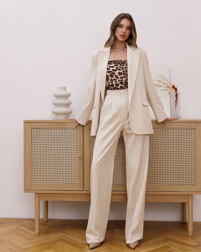 Woman in a beige suit with a leopard print top standing in front of a wooden cabinet.