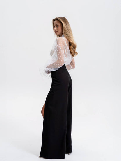 Woman wearing a white sheer top and black pants on a white background